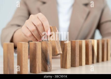 Versicherung mit Händen schützt Domino. Geschäftsmanns Hände verhindern, dass Dominosteine in die Hauskrise fallen. Kontrolle und Planung von Geschäftsrisiken sowie Strategien für die Durchführung Stockfoto