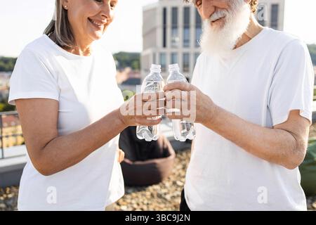 Seniorenpaar, das Wasserflaschen toast und einen gesunden Lebensstil im Freien genießt Stockfoto