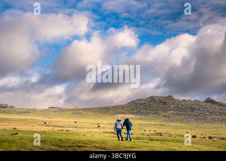 Zwei Personen gehen auf den imposanten Granitgrat Roughtor Rough Tor auf dem wilden windgepeitschten Bodmin Moor in Cornwall in Großbritannien. Stockfoto