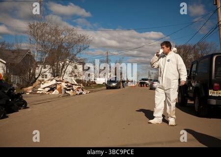 Ein Mann in einem Anzug für Gefahrstoffe trinkt Kaffee, der von Freiwilligen bereitgestellt wird, während er eine Straße mit Trümmern und Trümmern entlang läuft, die Superstorm Sandy in Union Beach NJ hinterlassen hat Stockfoto