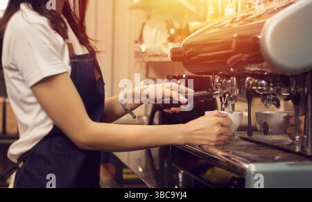 Hände des Baristas, der Kaffee mit einer Espressomaschine zubereitet. Barista Frau mit Schürze bereitet Kaffee für Gäste in ihrem kleinen Unternehmen vor Stockfoto