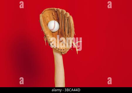 Hand in Leder Baseballhandschuh hält weißen Baseball auf rotem Hintergrund. Hochwertige Fotos. Gewinner. Kopierbereich Stockfoto