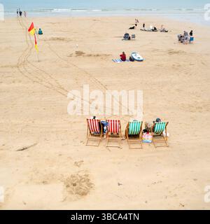 Urlauber Besucher sitzen in Liegestühlen am Towan Beach in Newquay in Cornwall in Großbritannien Stockfoto