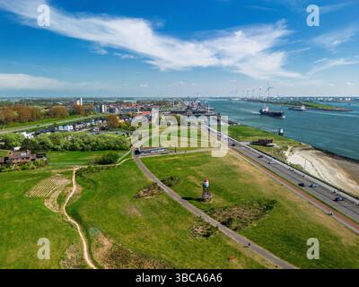 Aus der Vogelperspektive auf eine Küstenstadt mit grünen Parks, Wohngebieten, einer Flussstraße und belebten Schifffahrtsstraßen. Windturbinen und Industriehafen Stockfoto
