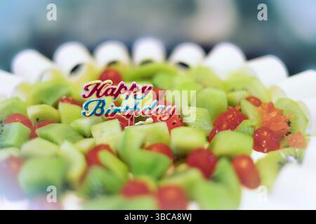 Geburtstagskuchen Nahaufnahme. Happy Birthday Obstkuchen dekoriert mit Kirschen und Kiwi. Alles Gute zum Geburtstag auf dem Kuchen. Selektiver Fokus, blu Stockfoto