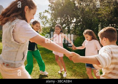 Eine Gruppe von Kindern, die Hände halten und gemeinsam in einem sonnigen Park spielen, fördert Freundschaft und Outdoor-Spaß. Stockfoto
