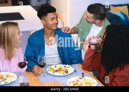 Gruppe von multiethnischen Freunden, die gemeinsam Abendessen und Wein am heimischen Tisch genießen Stockfoto
