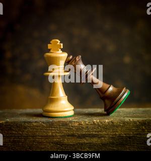 Zwei aufwendig gestaltete Schachfiguren, ein goldener König und eine dunkle Königin, lehnen sich auf einer alten Holzfläche gegeneinander und symbolisieren die strategische da Stockfoto