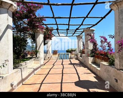 Von einer von Pergolen gesäumten Terrasse aus blickt man von einer Villa auf einem Hügel in Ravello, Italien, auf das schimmernde Mittelmeer. Stockfoto