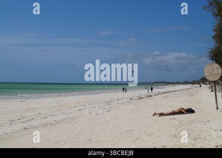 Ein paar Sonnenanbeter und Spaziergänger genießen die weite Strecke des weichen weißen Sandes und des türkisfarbenen Meeres am Diani Beach, Kenia. Stockfoto
