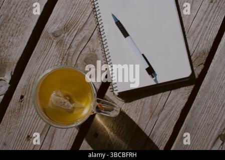 Ansicht von oben nach unten: Eine verpackte Teetasse und ein weißes Papierjournal, das mit leeren Seiten und einem Stift geöffnet ist Stockfoto