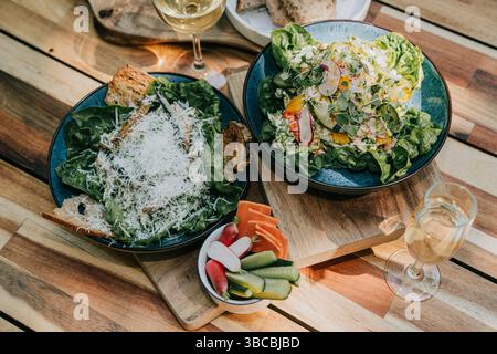 Ein Holztisch mit zwei Schüsseln Salat und einem Glas Wein. Der Salat ist eine Mischung aus Gemüse und Gemüse, und der Wein ist ein Weißwein Stockfoto