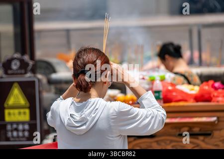 Sanya, Hainan Island, China. Frau, die im chinesischen Tempel rauchende Räucherstäbchen hält Stockfoto