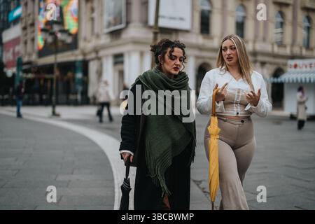 Zwei Frauen, die sich unterhalten, während sie draußen in einer urbanen Umgebung spazieren gehen Stockfoto