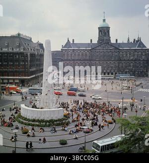 1960er Jahre, Blick auf den Dam-Platz, Amsterdam, Nordholland, die Niederlande, Menschen, die am nationalen Kriegsdenkmal sitzen. Die plaza wurde im 13. Jahrhundert erbaut, ihr Name stammt von dem Ort, an dem der erste Damm an der Amstel errichtet wurde. Der Platz befindet sich in der Altstadt und ist von historischen Gebäuden umgeben, darunter dem Königspalast. Stockfoto