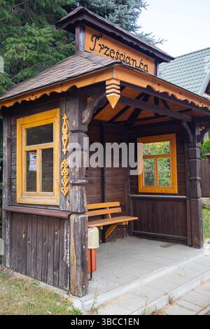 Vor einem Gebäude befindet sich eine kleine Holzkonstruktion mit einem gelben Dach und einem Schild mit der Aufschrift „Trezscianka“. Die Struktur hat eine Bank und zwei Fenster. Stockfoto