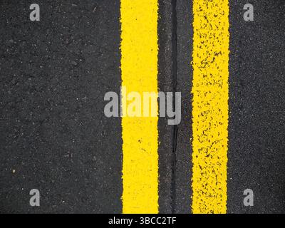 Nahaufnahme gelber Trennlinien auf der Straße mit Kopierraum. Gelbe doppelte durchgezogene Linie. Straßenmarkierungen auf Asphalt. Grauer Asphalthintergrund mit zwei Yello Stockfoto