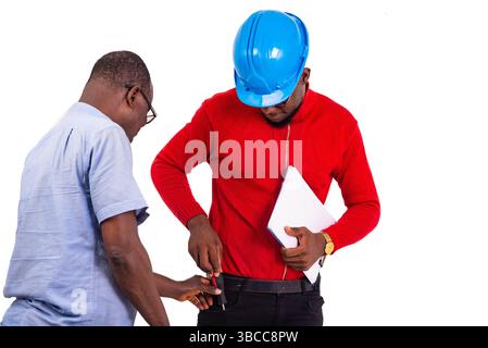 Mann in blauem Hemd hilft dem jungen Ingenieur, einen Schraubenzieher in seine Hosentasche zu stecken oder zu nehmen. Stockfoto