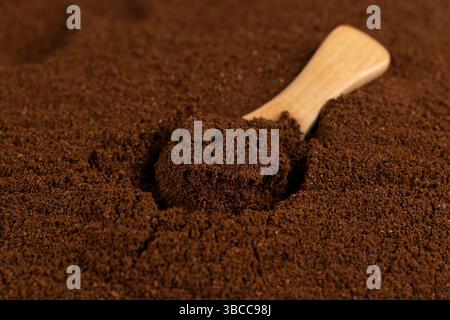 Gemahlener Kaffee und ein kleiner Holzlöffel, eine große Anzahl gerösteter gemahlener Kaffeebohnen in Pulver und ein Holzlöffel Stockfoto