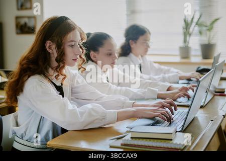 Mädchen folgen aufmerksam dem Unterricht, während sie im Klassenzimmer an Computern arbeiten und gemeinsam mit ihren Mitschülern an fleißigen Aktivitäten teilnehmen Stockfoto