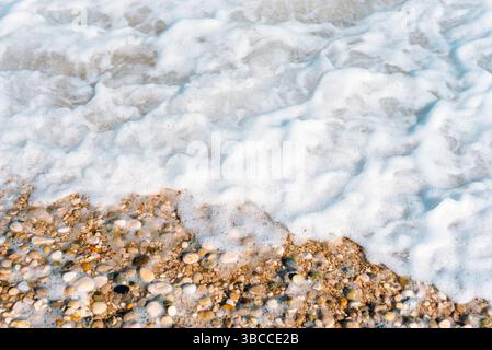 Meeresschaum, der sanft über glatte Kieselsteine an einer ruhigen Küste wäscht, fängt die natürliche Textur und die Ruhe der Küste ein. Natürlicher Hintergrund, Draufsicht. Stockfoto