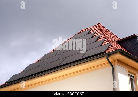 Solarpaneele sind in ein rot gekacheltes Dach eines Wohnhauses unter bewölktem Himmel integriert. Stockfoto
