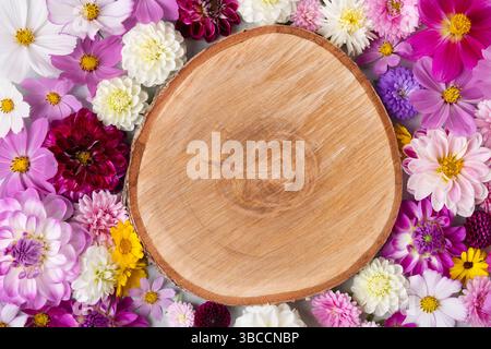 Runder, strukturierter Holzabschnitt für die Präsentation von Kosmetikprodukten leeres Modell mit Blumen. Minimalistischer flacher Hintergrund, Draufsicht. Stockfoto