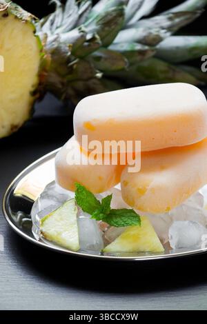 Ananassorbet-Eis-Eis-Eis auf Silberplatte mit Eiswürfeln gehackte Ananasscheiben, Minze nahe in halbe Ananas auf schwarzem Hintergrund geschnitten. Ananassorbet-Eis-Eis. Vertikal. Stockfoto