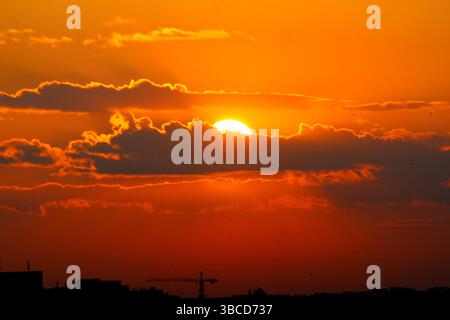Die Sonne untergeht hinter dramatischen Wolken über einer Skyline der Stadt und strahlt warme Orange- und Rottöne über den Himmel. Eine perfekte Mischung aus Natur und urbaner Atmosphäre Stockfoto
