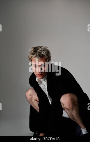 Porträt eines gutaussehenden jungen Mannes im Mantel, der auf dem Boden sitzt und in die Kamera blickt Stockfoto
