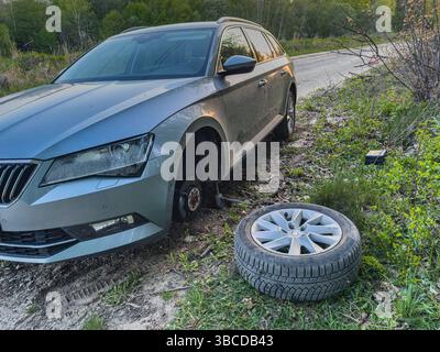 Lemberg Ukraine 04.21.25 Ein silbernes Auto sitzt am Rande einer Landstraße mit einem Platten Reifen, während das Reserverad in der Nähe im grünen Gras liegt. Groß Stockfoto