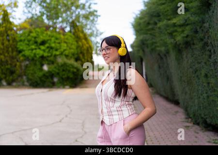 Junge Frau, die gelbe Kopfhörer trägt und draußen Musik hört Stockfoto