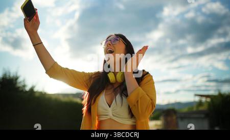 Aufgeregte junge Frau, die ihr Smartphone hält und draußen Musik genießt Stockfoto
