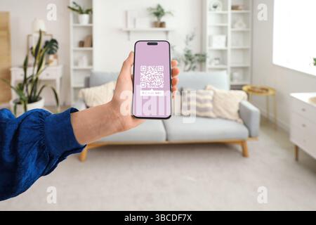 Frau, die zu Hause das Smartphone mit QR-Code in Nahaufnahme auf dem Bildschirm hält Stockfoto