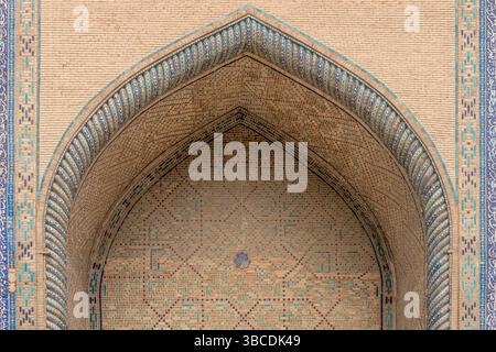 Ein spitzer Bogen mit verblassten Fliesen markiert die Fassade der Ulugbek Madrasah in Buchara, Usbekistan, ein dauerhaftes Timurid-architektonisches Erbe. Stockfoto