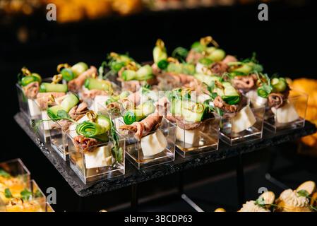 Gourmet-Hors d'oeuvres in kleinen, klaren Tassen mit gerollten Rindfleischscheiben, Gurkenbändern und Käsewürfeln. Stockfoto