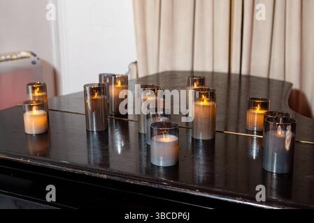 Gruppe moderner Glaskerzen, die sanft auf einem schwarzen Flügel leuchten und ein warmes und elegantes Ambiente schaffen. Stockfoto