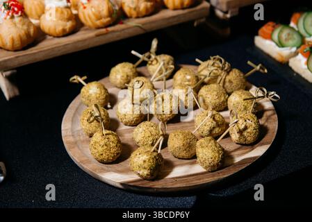 Appetitliche Präsentation von mundgroßen Käsebällchen, die mit zerstoßenen Pistazien beschichtet sind und auf Holzpflücken serviert werden, perfekt für Catering oder Partys. Stockfoto