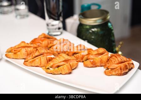 Frisch gebackene Mini-Croissants gefüllt mit Räucherlachs und Frischkäse, serviert auf einer weißen Platte für Catering oder Brunch. Stockfoto