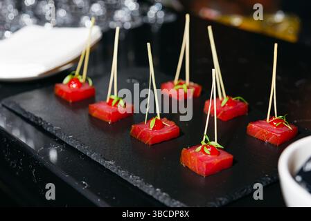 Elegante Thunfischhors d'oeuvres, serviert auf Spießen mit Ziergarnitur, die auf einer Platte aus schwarzem Schiefer für gehobene Veranstaltungen angeordnet sind. Stockfoto