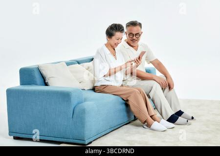 Ein älteres Ehepaar, das auf der Couch sitzt und ihre Telefone benutzt Stockfoto