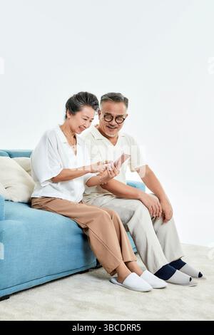 Ein älteres Ehepaar, das auf der Couch sitzt und ihre Telefone benutzt Stockfoto