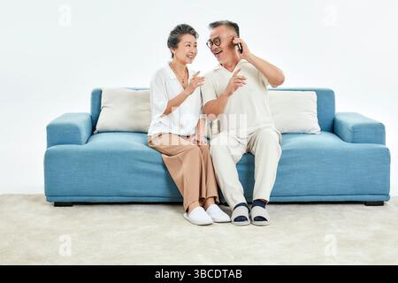Ein älteres Ehepaar, das auf der Couch sitzt und ihre Telefone benutzt Stockfoto