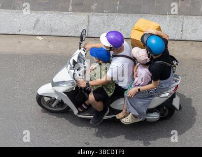 Eine vierköpfige Familie, darunter zwei Kinder, fährt gemeinsam auf einem einzigen Motorrad auf einer urbanen Straße in Vietnam Stockfoto
