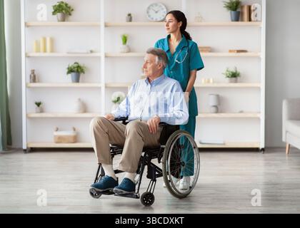 In voller Länge Porträt von älteren männlichen Patienten im Rollstuhl und Seine junge Pflegekraft im Altersheim Stockfoto