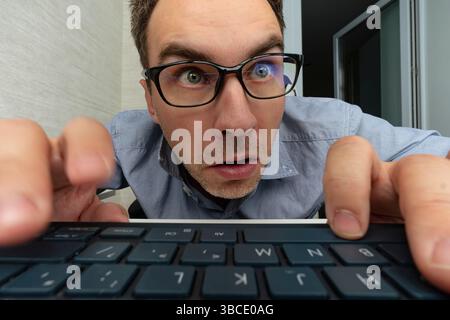 Junger überraschter Texter-Geek-Software-Ingenieur IT-Spezialprogrammierer Mann in blauem Hemd Touchbrille arbeiten im Büro, schreiben Code-Typ-Skript auf Stockfoto