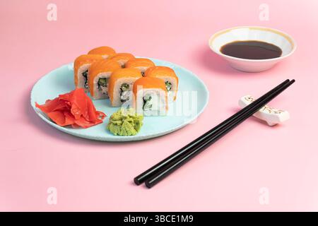 Sushi rollt philadelphia auf einem blauen Tellerständer auf rosa Hintergrund. wasabi Ingwer und Soße Essstäbchen. Brötchen mit Lachs, Frischkäse, Avocado. bri Stockfoto
