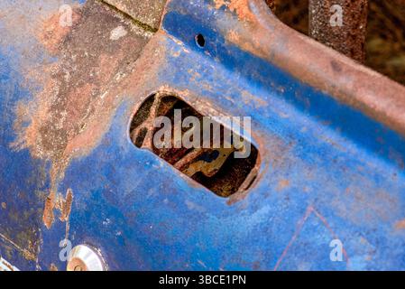 Nahaufnahme einer rostblauen Rennwagentür mit abblätternder Farbe und freiliegendem inneren Verriegelungsmechanismus, der den Verfall und die Vernachlässigung von Vintage unterstreicht. Stockfoto