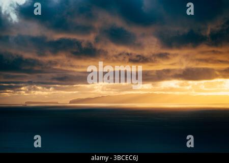 Dramatischer Sonnenuntergang über dem Ozean mit dunklen Wolken und goldenem Licht, das durchbricht Stockfoto