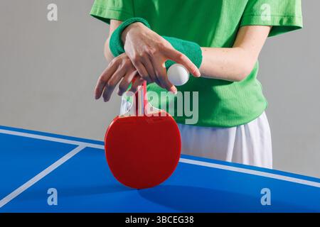 Tischtennisspieler in Grün, der sich auf das Servieren vorbereitet, Tischtennispong Paddle und Ball auf einem blauen Spieltisch hält. Stockfoto